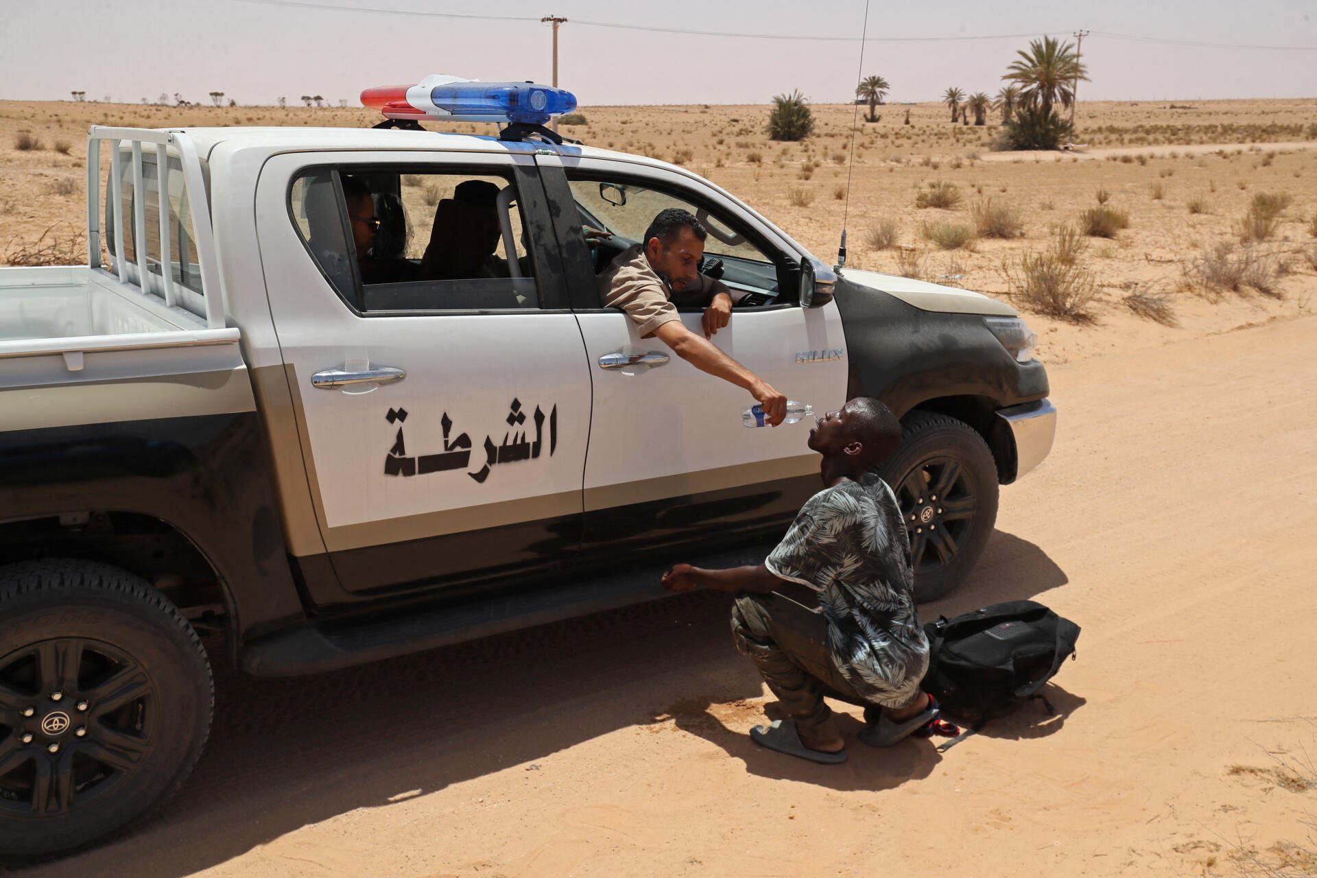 Un garde-frontière Libyen donne de l'eau à un migrant durant une opération de sauvetage dans une one inhabité près  de la frontière de la ville d'Al-Assah le 16 Juillet 2023. Les gardes-frontière ont secouru une douzaine de migrants qui ont selon eux été abandonnés dans le désert par les autorités Tunisiennes sans eau, nourriture ou abri. @Mahmud Turkia/AFP 