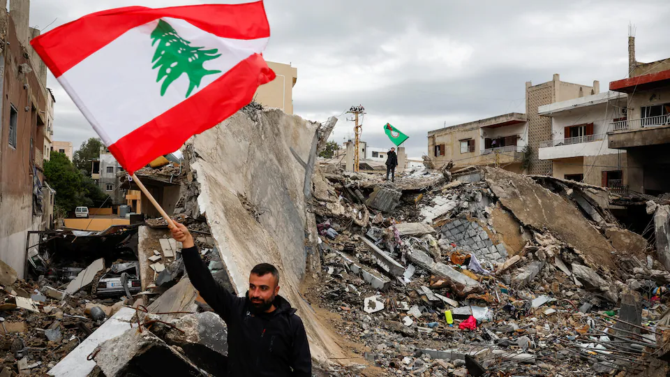 Un homme brandissant le drapeau libanais devant un immeuble anéanti par un bombardement israélien dans la ville de Tyr, dans le sud du Liban, le 27 novembre 2024.

Photo : Reuters / Adnan Abidi