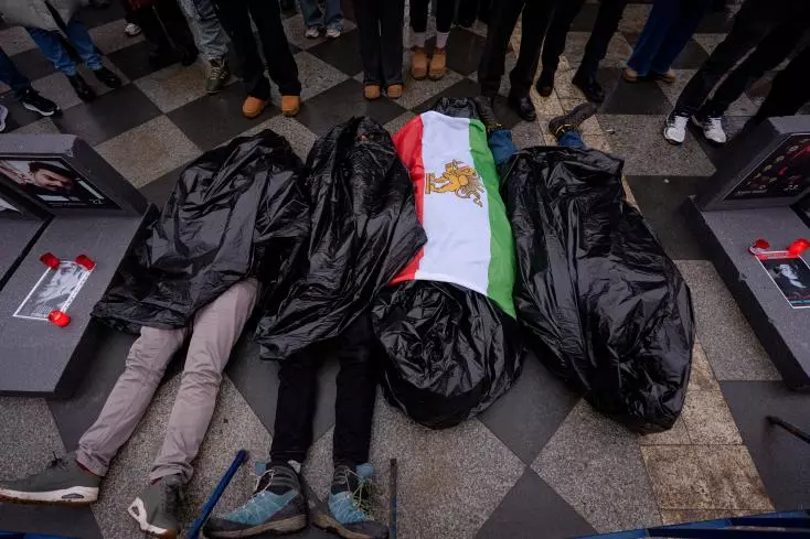 Des personnes recouvertes de sacs plastique symbolisant des victimes sont allong&eacute;es sur le trottoir lors d'un rassemblement de soutien aux manifestations anti-gouvernementales en Iran, &agrave; Bucarest, Roumanie, samedi 24 janvier 2026.
